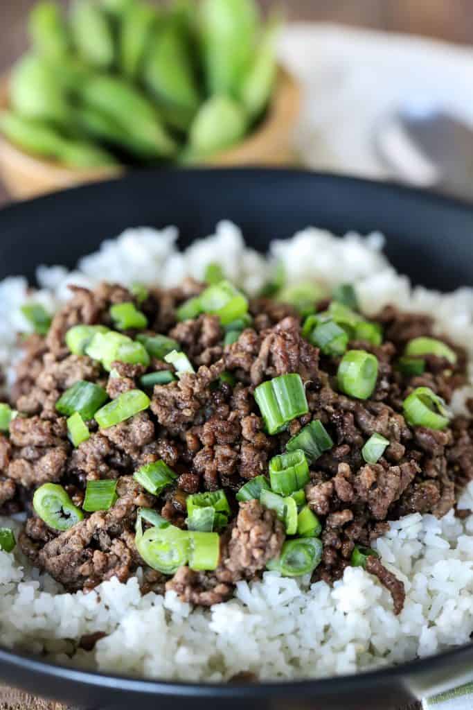 A plate of Korean beef on a bed of white rice, topped with chopped green onions.