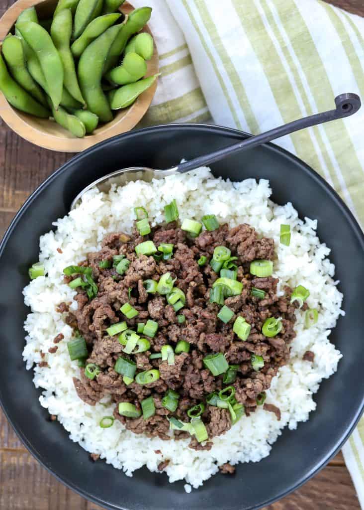 Overhead view of a plate of Korean beef on white rice, topped with chopped green onions.
