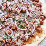 Homemade Grilled BBQ Chicken Pizza with a no-rise homemade crust and topped with grilled chicken, BBQ sauce, red onion, cilantro & mozzarella on a piece of parchment paper.