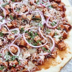Homemade Grilled BBQ Chicken Pizza with a no-rise homemade crust and topped with grilled chicken, BBQ sauce, red onion, cilantro & mozzarella on a piece of parchment paper.