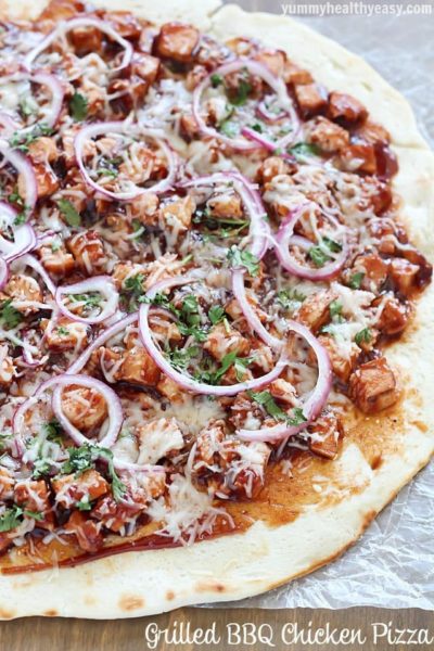 Homemade Grilled BBQ Chicken Pizza with a no-rise homemade crust and topped with grilled chicken, BBQ sauce, red onion, cilantro & mozzarella on a piece of parchment paper. 
