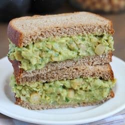 Avocado Chickpea Salad Sandwiches stacked on top of eathother on a white plate.
