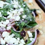 Easy Greek Pizza Recipe with a mayo & garlic spread and topped with feta, red onion, spinach, sun dried tomatoes and kalamata olives. Crazy delicious!