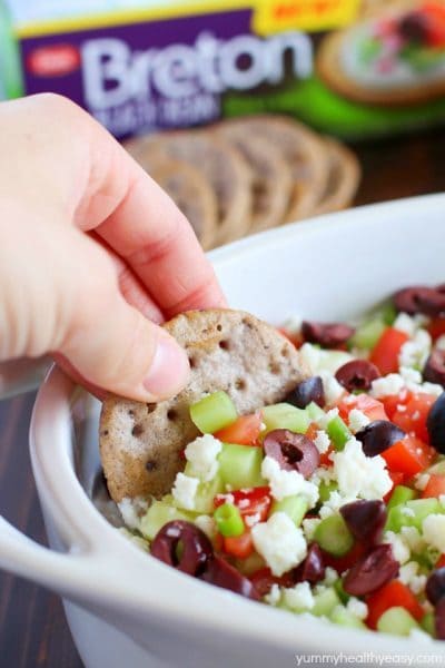 Cracker is dunked into a Healthy Greek Dip, made with cottage cheese then topped with cucumbers, green onions, tomatoes, kalamata olives, and feta cheese.