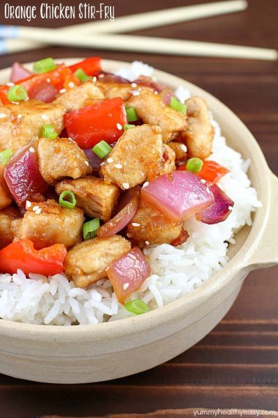 The most incredible Orange Chicken Stir Fry with pan seared chicken, red bell peppers, onion and a delicious sweet and savory sauce served over rice in a cute bowl and chopsticks in the background!