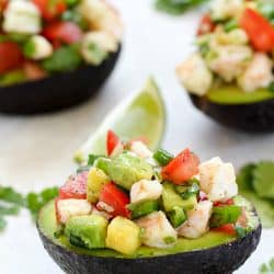 Three Avocados filled with Shrimp Ceviche on a counter with a lime garnish.