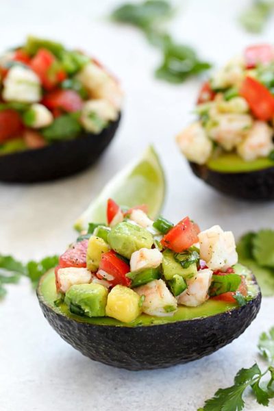 Three Avocados filled with Shrimp Ceviche on a counter with a lime garnish.