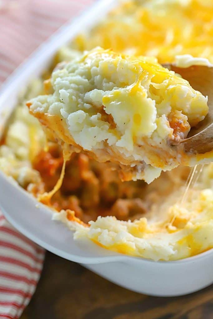 Shepherd's Pie in a casserole dish with a wood spoon pulling up a big spoonful.