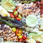 Deconstructed Cobb Salad on platter with marinated and grilled chicken, grilled romaine and other Cobb salad ingredients.