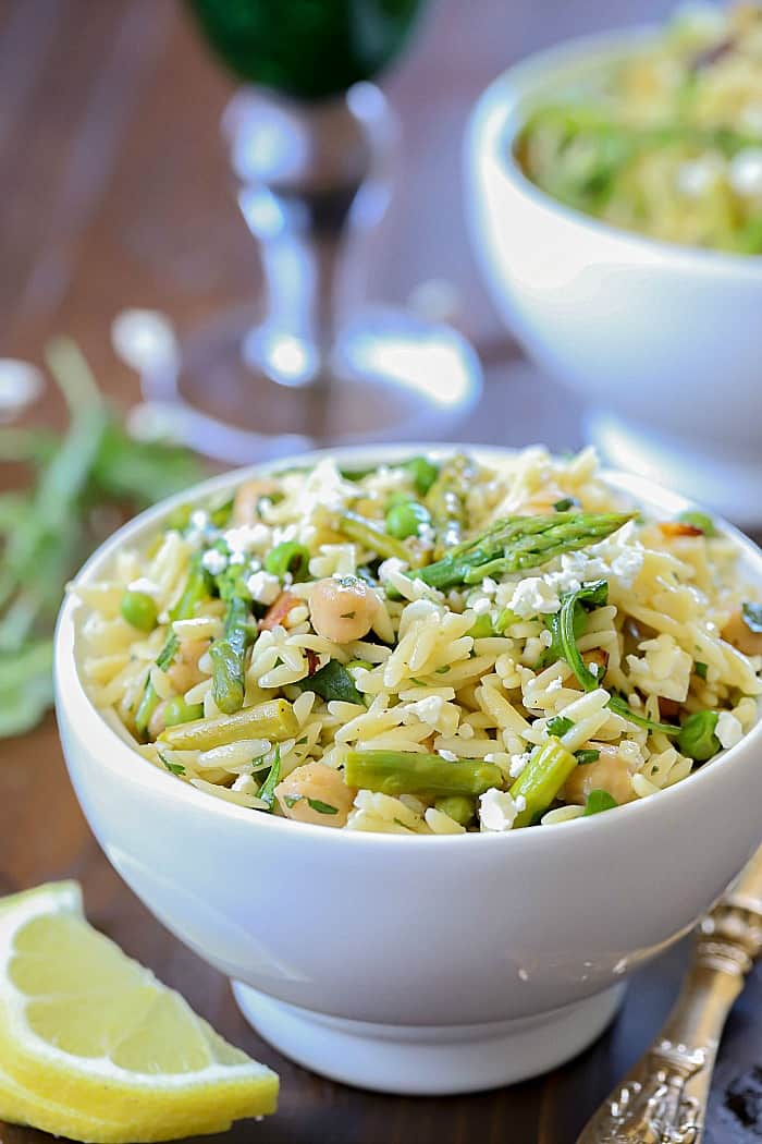 Close up view of a beautiful salad filled with orzo, asparagus, toasted almonds, arugula, feta cheese and peas with a vinaigrette.