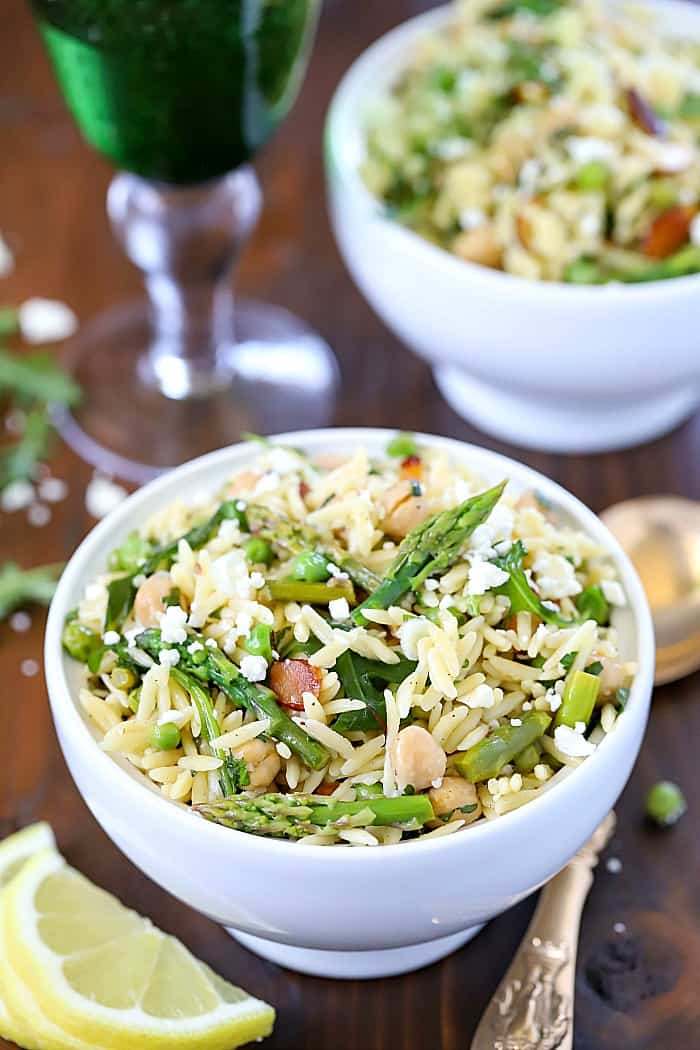 Top view of a beautiful Spring Orzo Salad filled with orzo, asparagus, toasted almonds, arugula, feta cheese and peas with a vinaigrette.