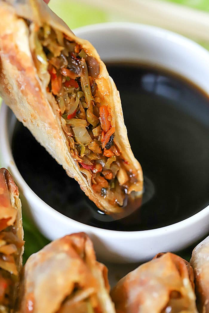 Close up view of a sliced in half egg roll being dipped into soy sauce.