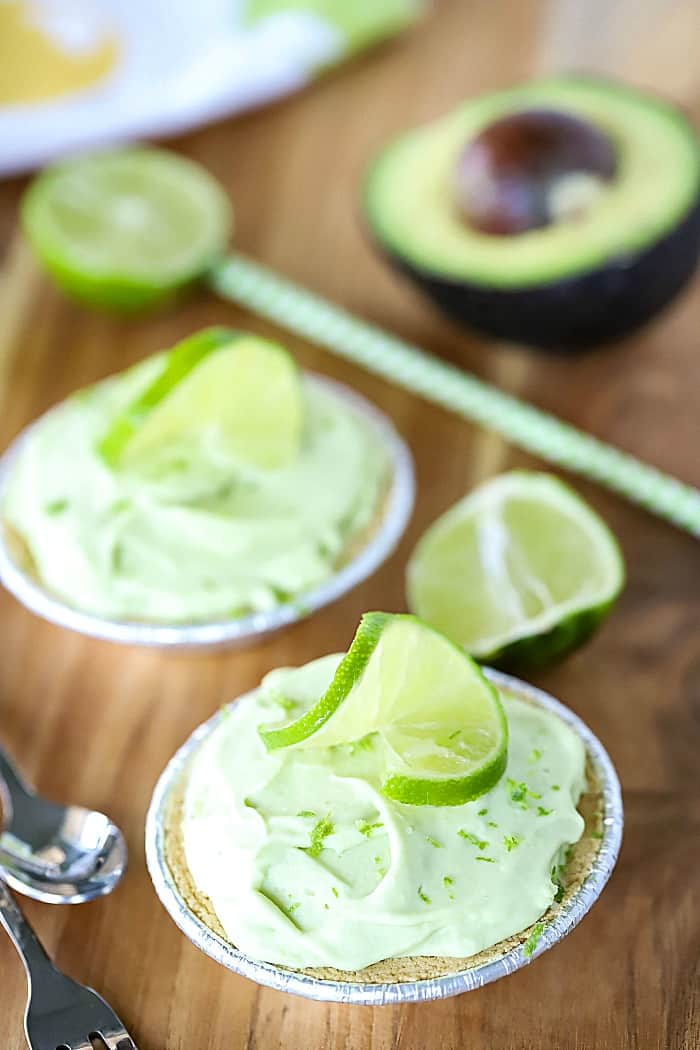Photo of two mini key lime pies with lime and avocado in the background.