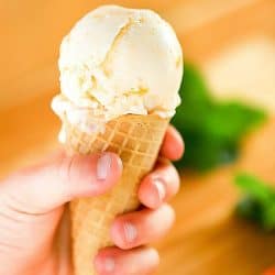 Child's hand holding a waffle ice cream cone filled with peach frozen yogurt.