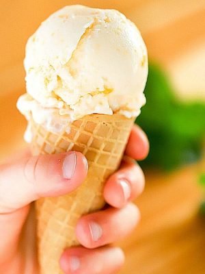 Child's hand holding a waffle ice cream cone filled with peach frozen yogurt.