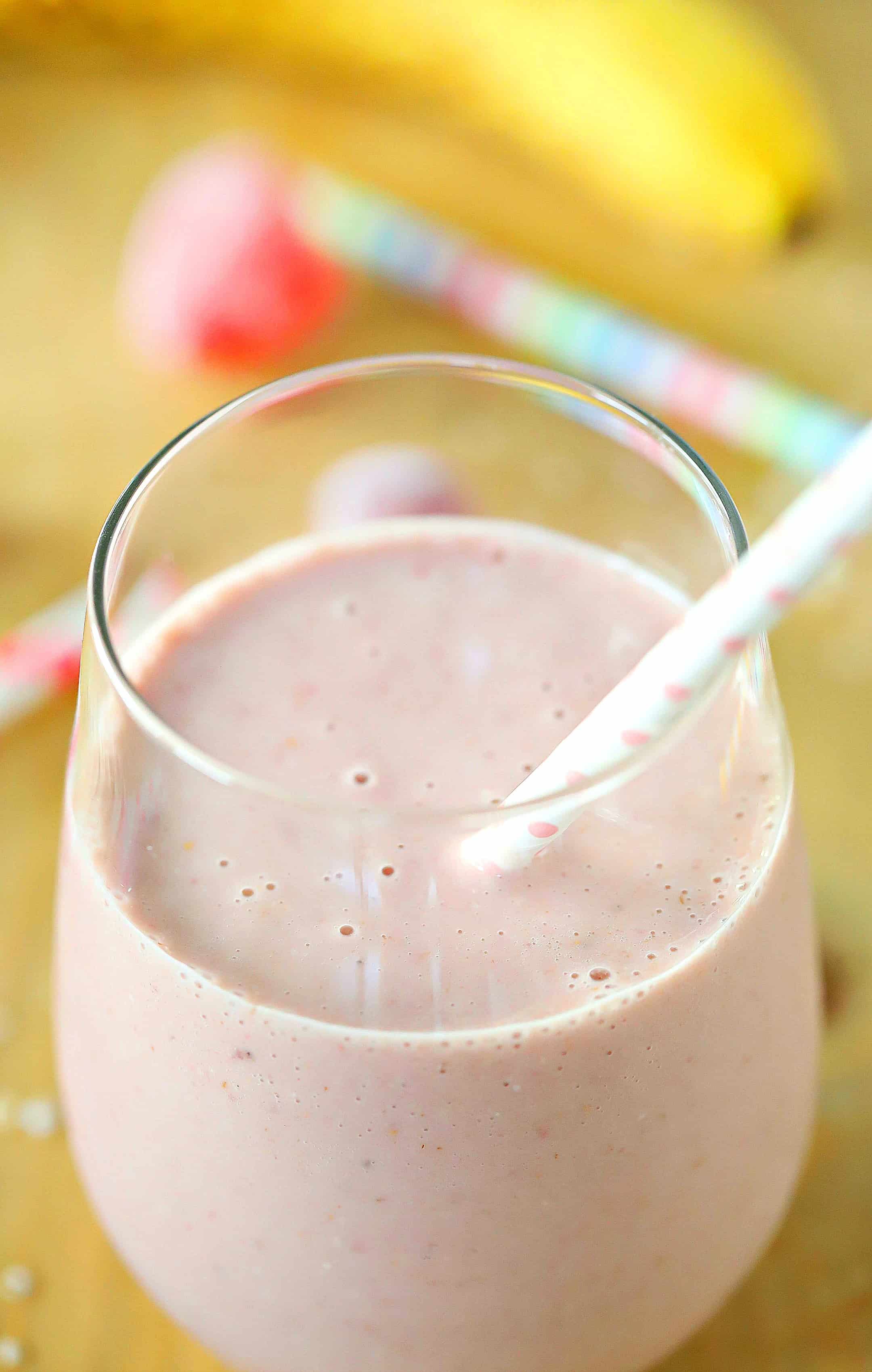 Photo of a strawberry oatmeal smoothie with a straw inside the glass cup.
