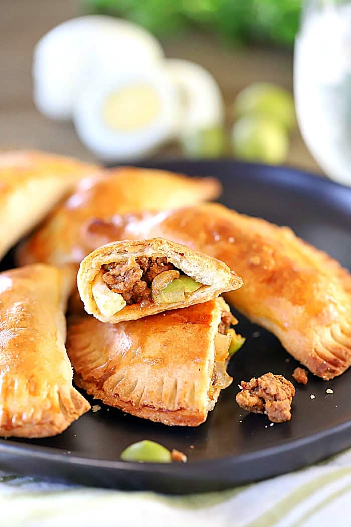 One plate of cooked beef empanadas with one in the front that's been cut in half