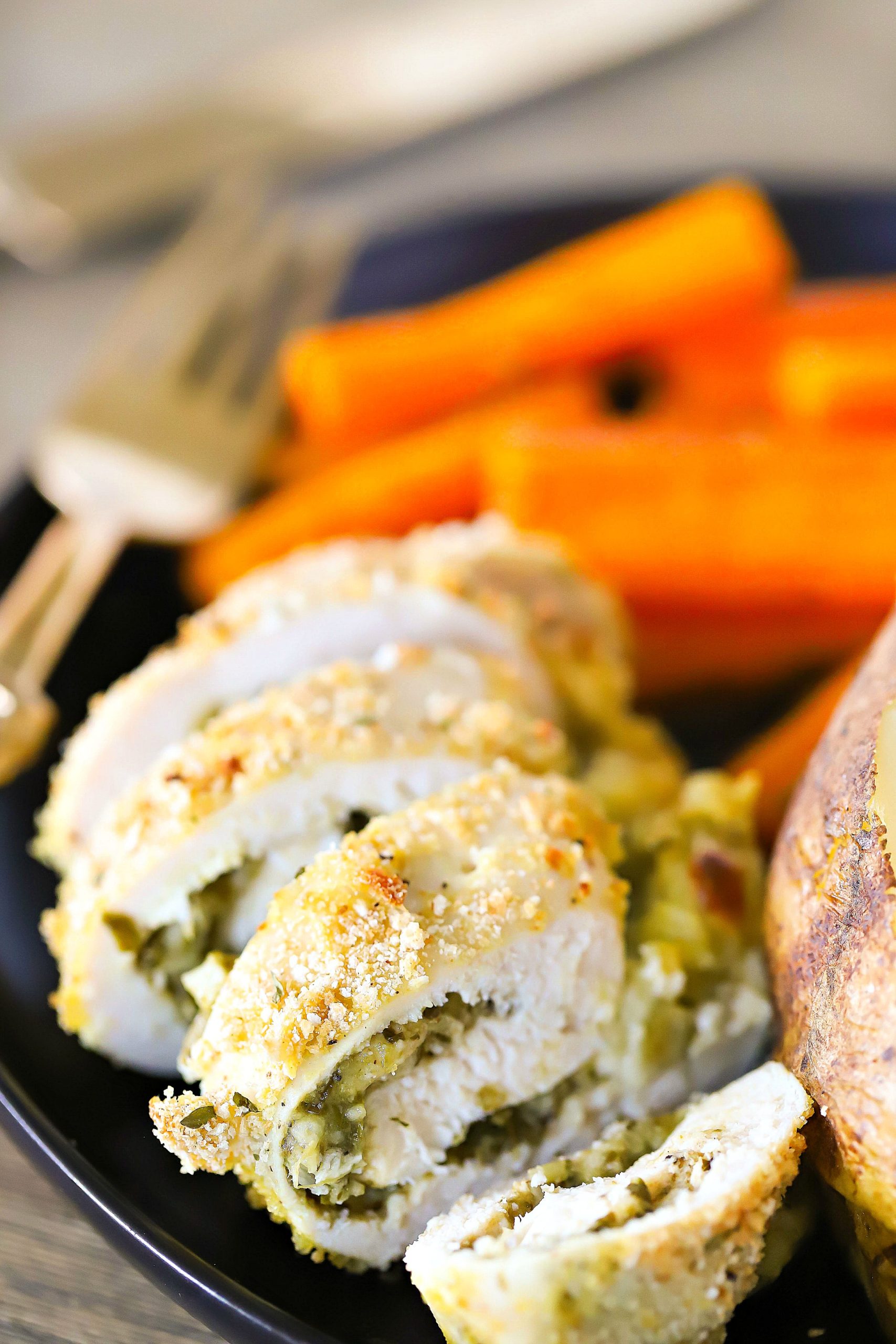 Sliced Pesto Stuffed Chicken on a black plate with a side of carrots and baked potato