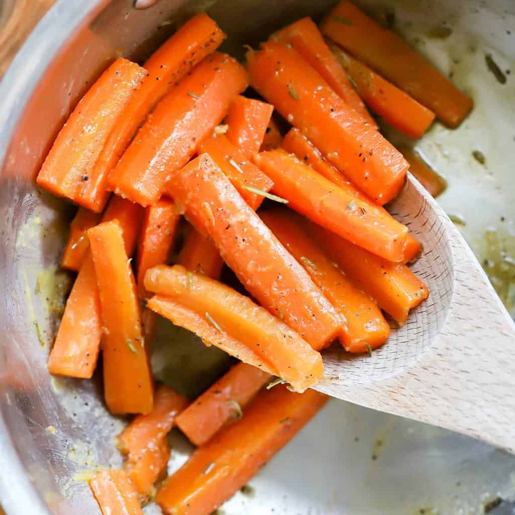 pan filled with cooked carrots and a large wooden spoon.