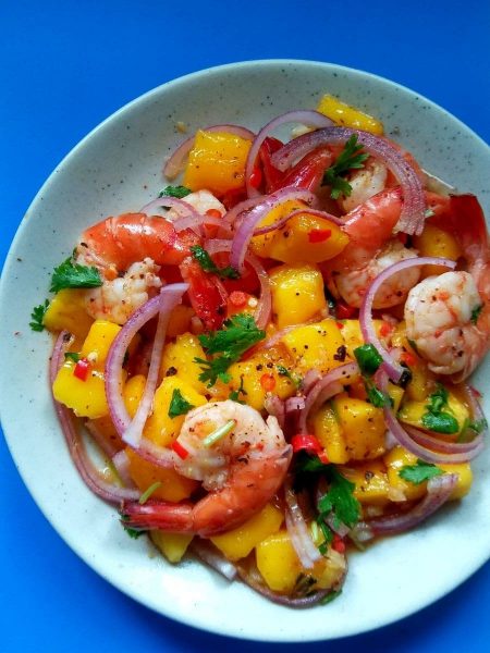 Delicious bowl of prawn and mango salad with a topping of red onion and parsley.