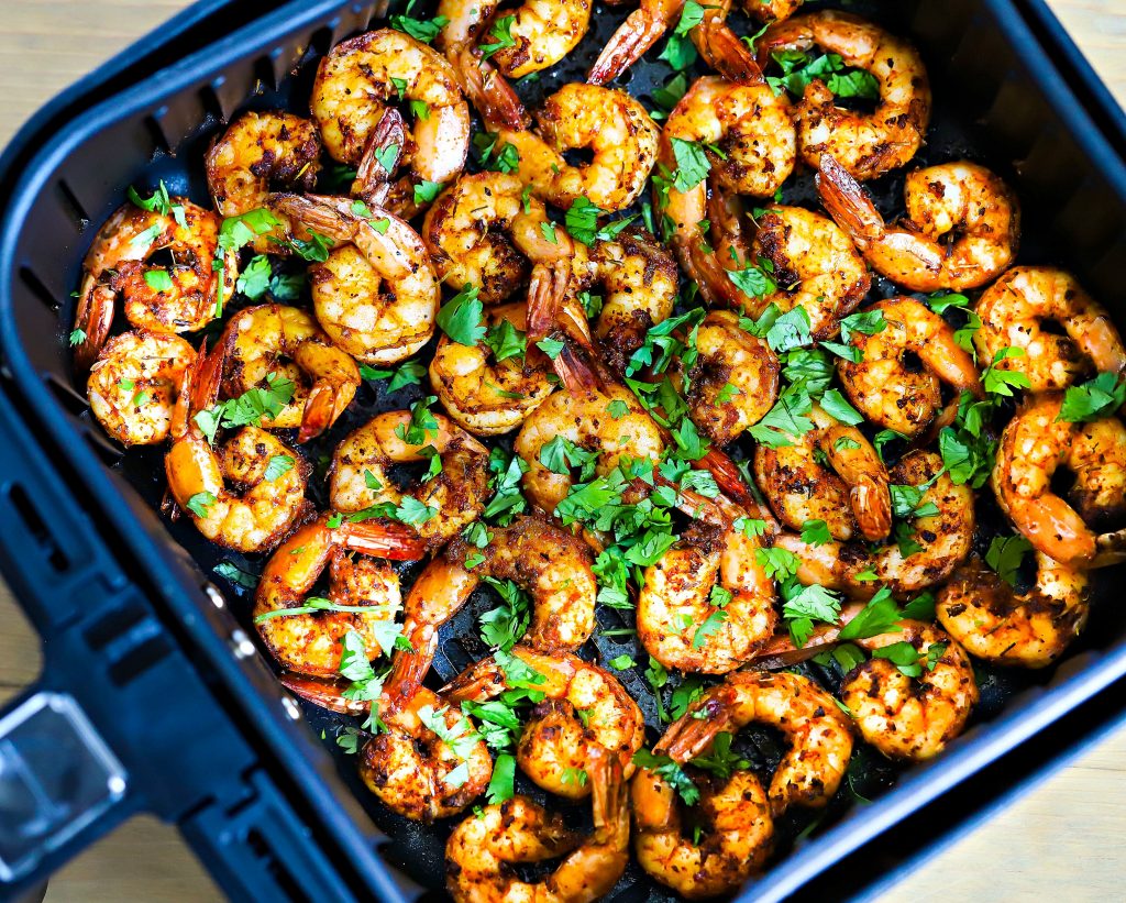 Air fryer basket filed with cooked spicy shrimp, topped with chopped cilantro.