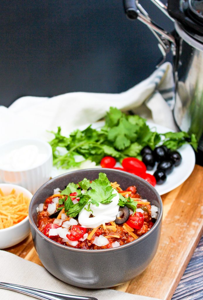 Small bowl of chili with toppings on it and toppings in the background.