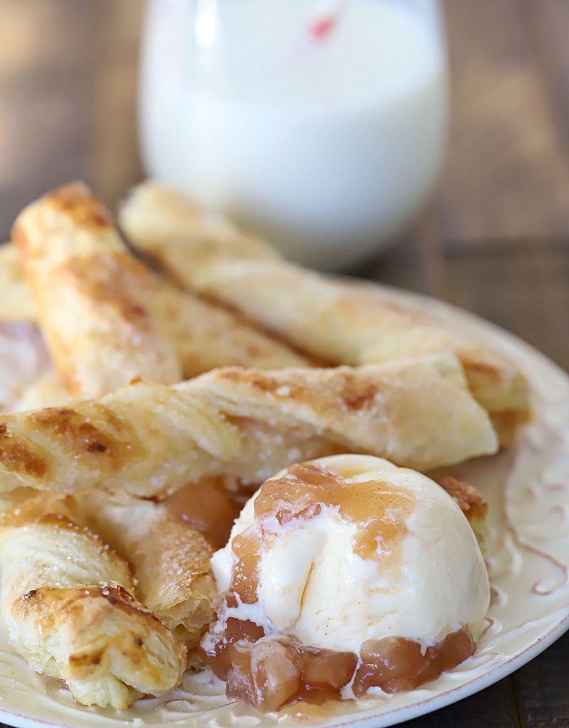 A plate full of strudel breadsticks with a side of vanilla ice cream topped with apple pie filling.