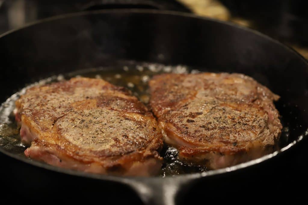 Two ribeyes cooking in a cast iron skillet