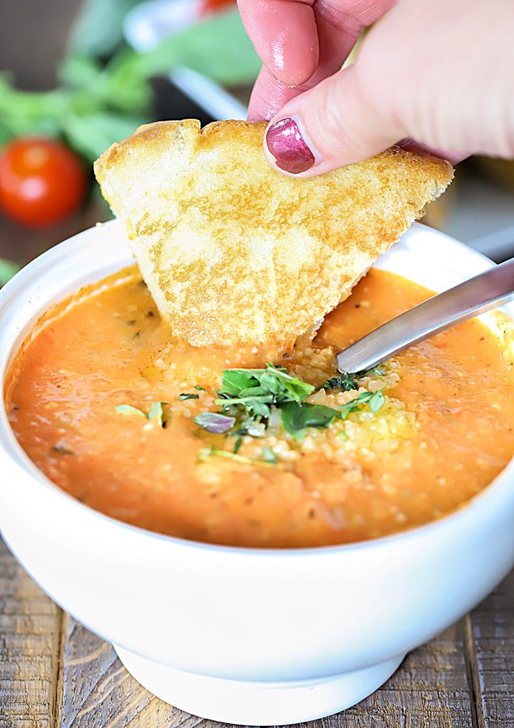 Grilled cheese is dunked in a bowl of tomato soup.